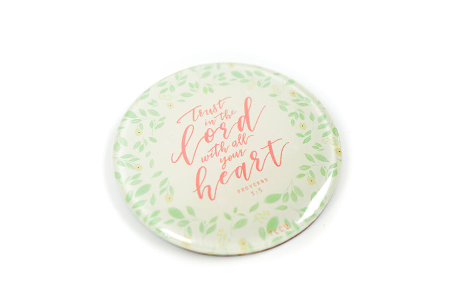 Close up of 5.5 cm diameter circular Acrylic fridge magnet with bible verse “Trust in the Lord with all your heart” on foliage background.