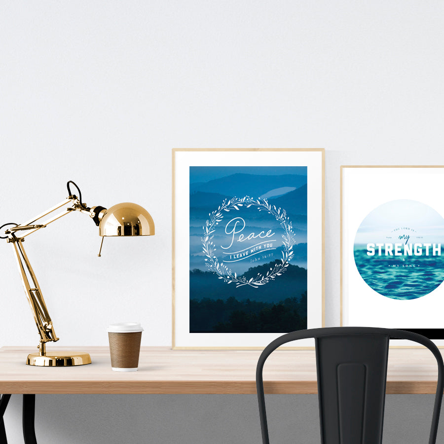 A3 beautiful painting poster placed standing next to a smaller A4 sized painting poster on a wooden table. Modern home interior design ideas. Blue theme.